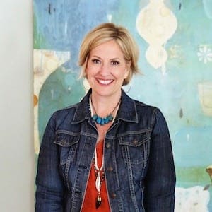 Portrait of Brené Brown, smiling, in front of an abstract painting