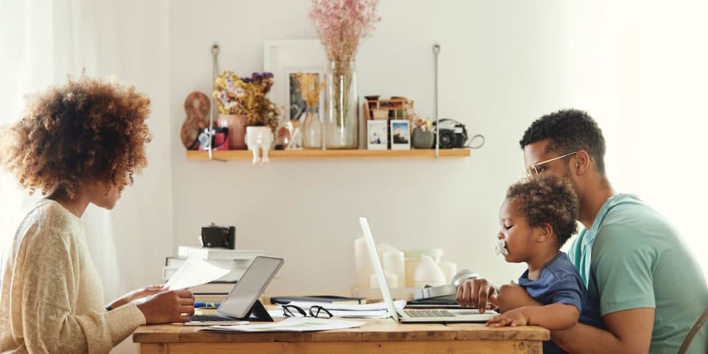 Mother using digital tablet to work from home while Father and son use laptop. They are sitting at the kitchen table