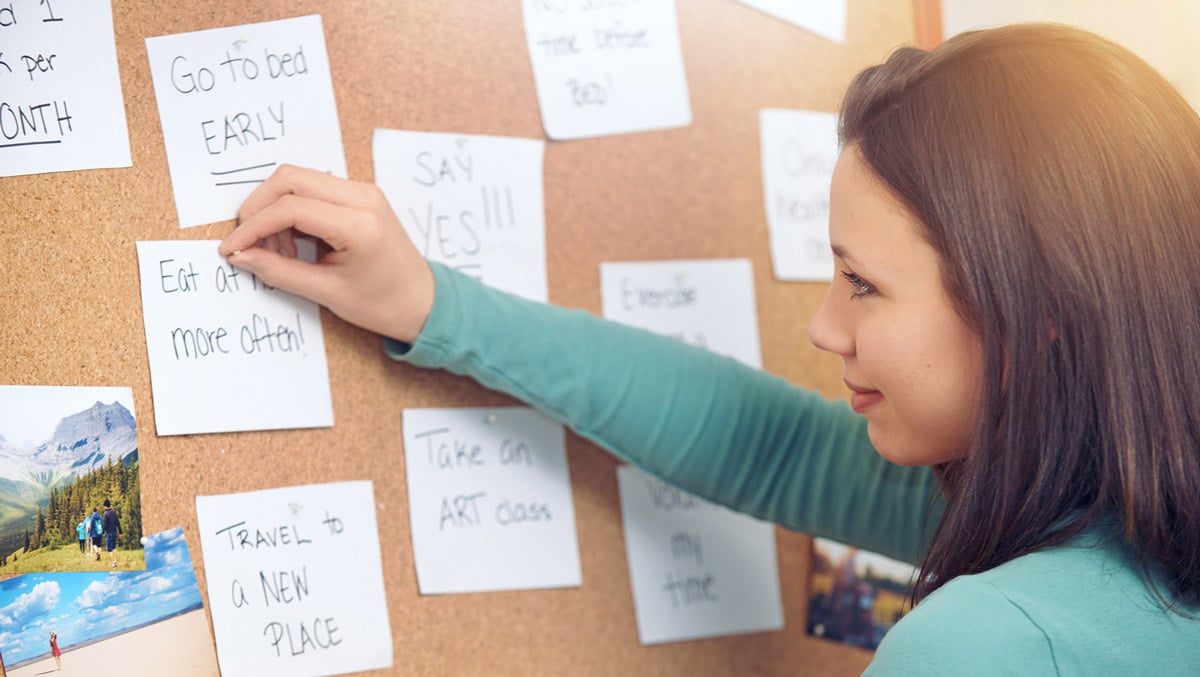 young woman pinning notes on a bulletin board to keep track of plans