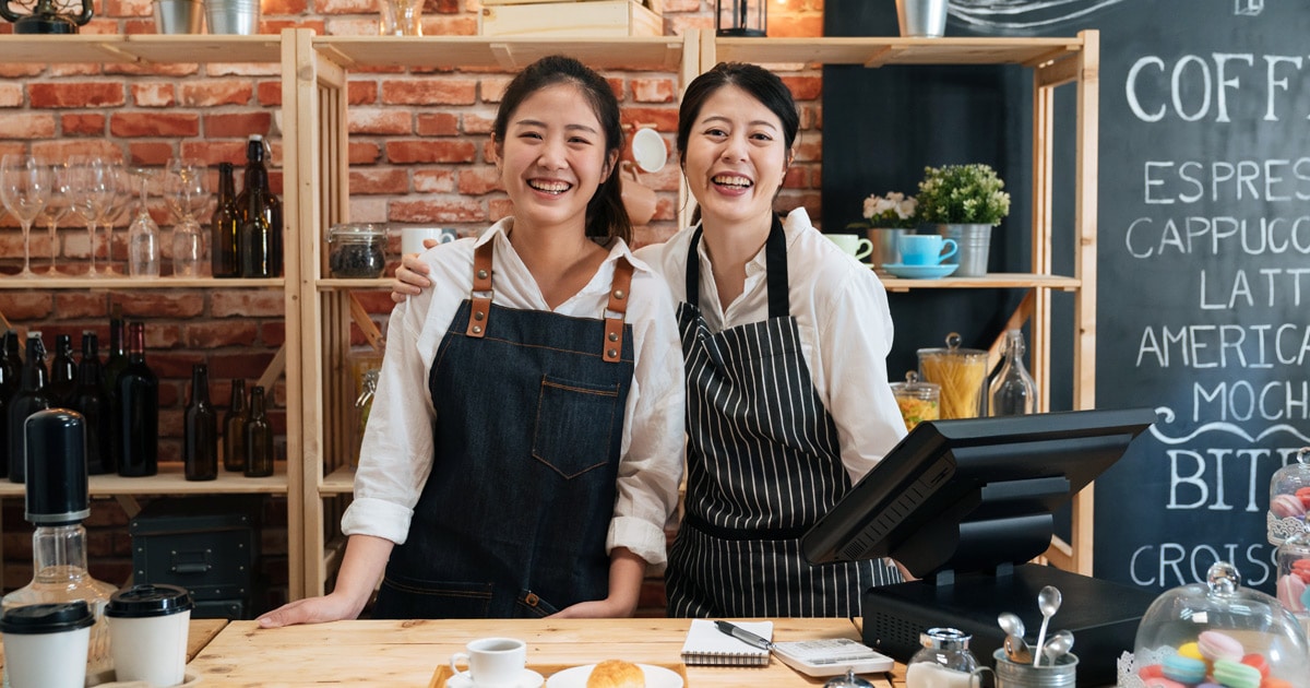 two Asian female baristas smiling while standing behind the counter of a women-owned coffee shop